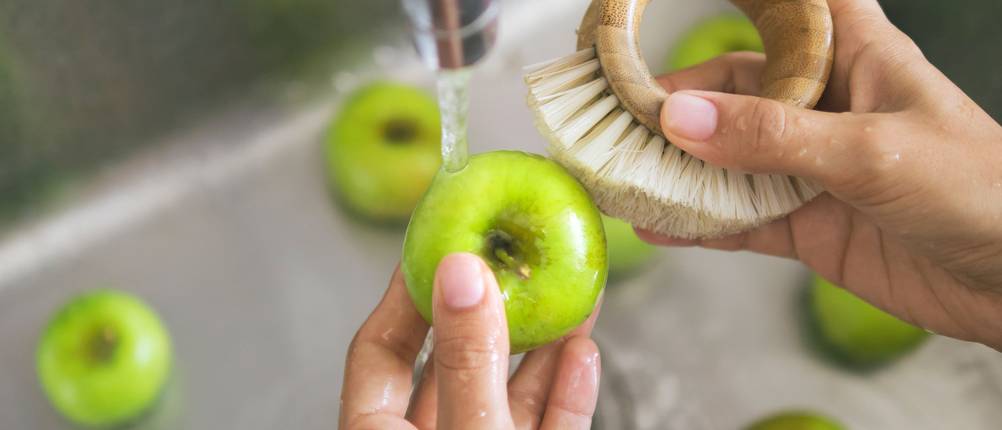Gemüsebürste-Test: Ein Apfel wird mit einer Bürste unter fließendem Wasser gereinigt.