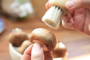 Gemüsebürste-Test: Eine Person putzt mit einer Pilzbürste einen Champignon.