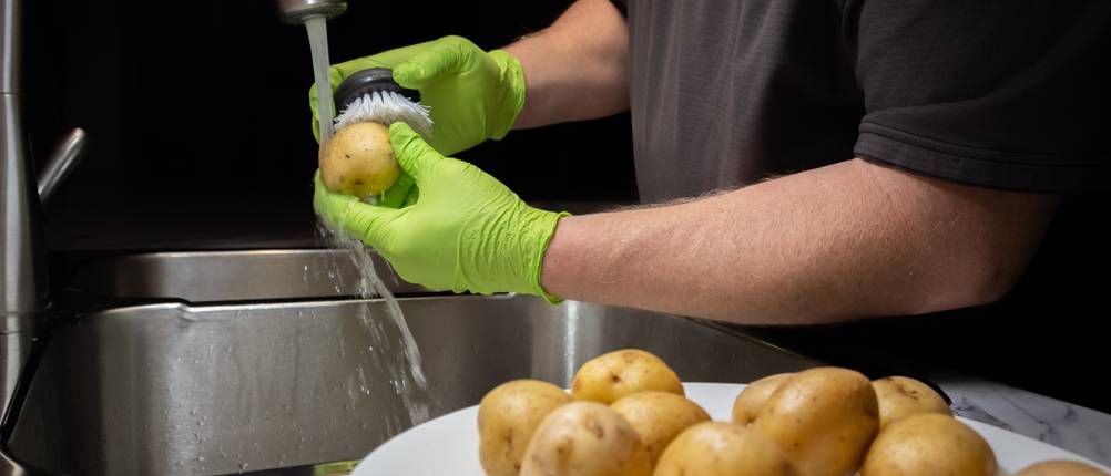 Gemüsebürste-Test: Eine Person putzt Kartoffeln unter fließendem Wasser.