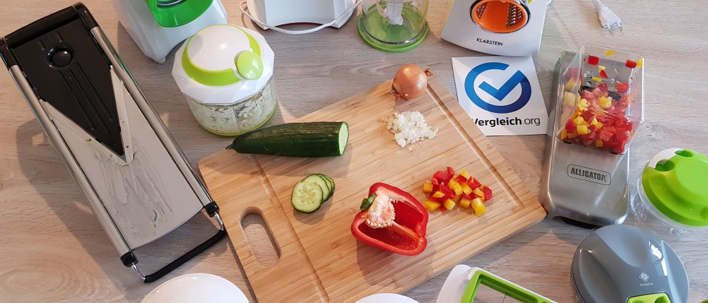 verschiedene Gemüseschneider im Test liegen neben einem Holzbrett mit Gemüse