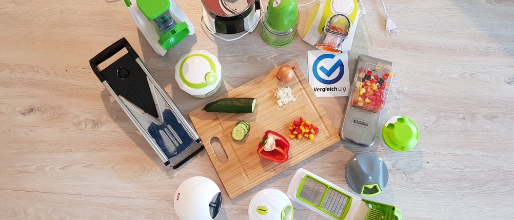 verschiedene Gemüseschneider mit verschiedenen Schneideinsätzen im Test auf einem Holztisch, daneben liegt vorbereitetes Gemüse auf einem Holzbrett