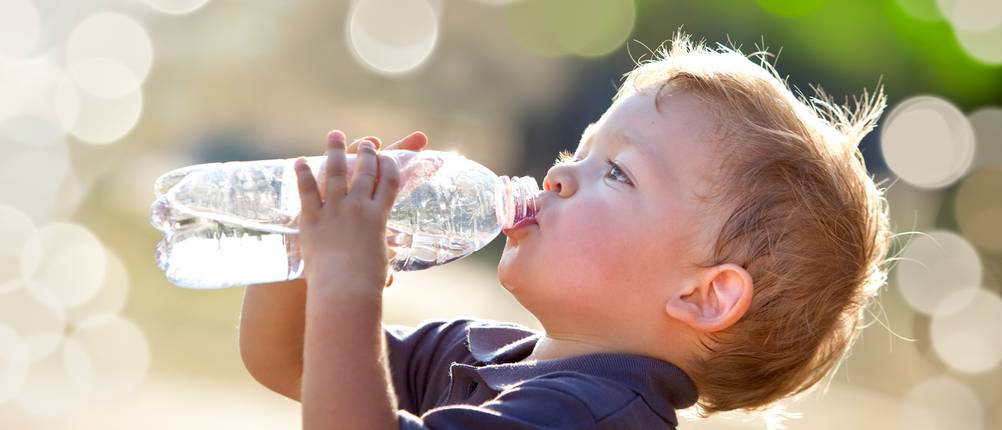 Kleiner Junge trinkt draußen Wasser aus einer Plastikflasche.