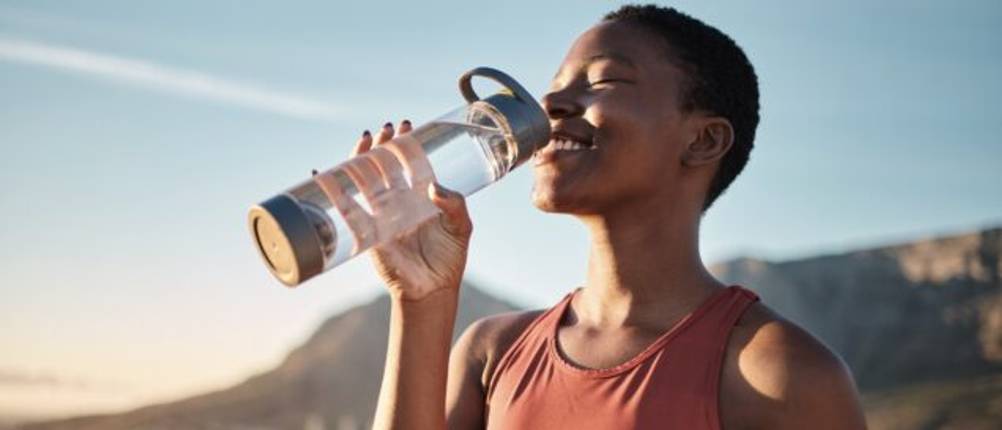 Frau macht eine Pause beim Joggen und trinkt Wasser aus einer durchsichtigen Flasche.