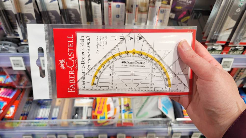 Eine Hand hält das getestete Geodreieck vor ein Regal.