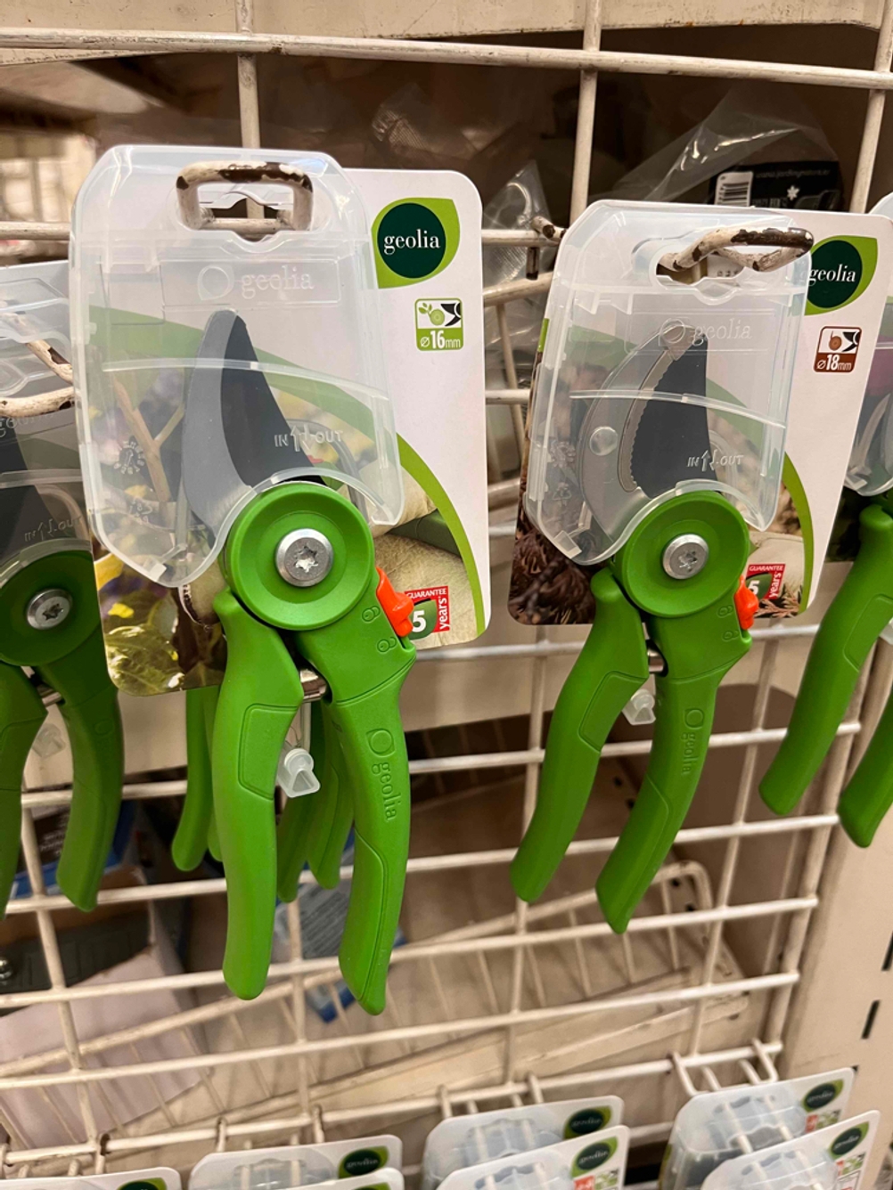 Mehrere verpackte Gartenscheren hängen zum testen in einem Gitterregal.