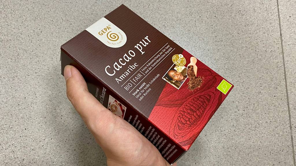 Bio Kakaopulver im Test: Hand hält eine Packung Cacao pur von Gepa schräg vor hellem Hintergrund.