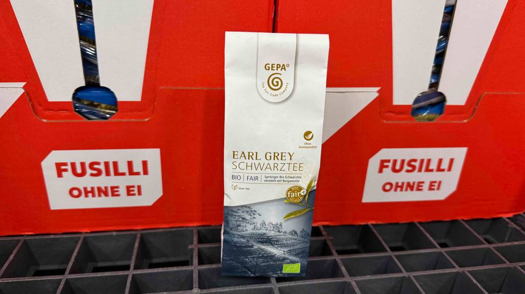 Bio-Schwarztee im Test in einer Verpackung der Marke Gepa steht vor roten Kartons mit Nudeln.