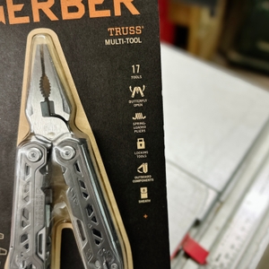 Die Verpackung des Gerber Truss Multitools zeigt eine Nahaufnahme der Zange sowie die wichtigsten Funktionen, darunter 17 integrierte Werkzeuge. Die Verpackung hebt die Schmetterlingsöffnung und federbelasteten Zangen hervor.
