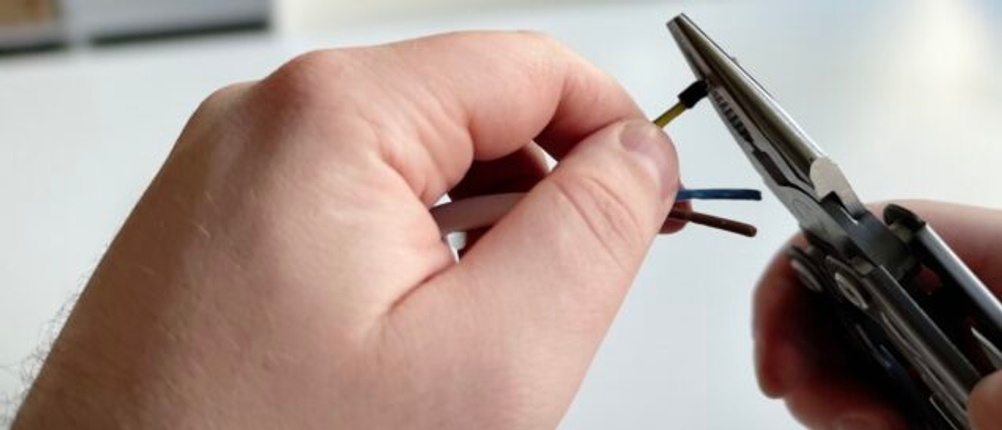 Eine Hand hält das Gerber Multitool, während mit der Zange ein Kabel gecrimpt wird. Der Hintergrund zeigt einen weißen Tisch mit moderner Einrichtung.