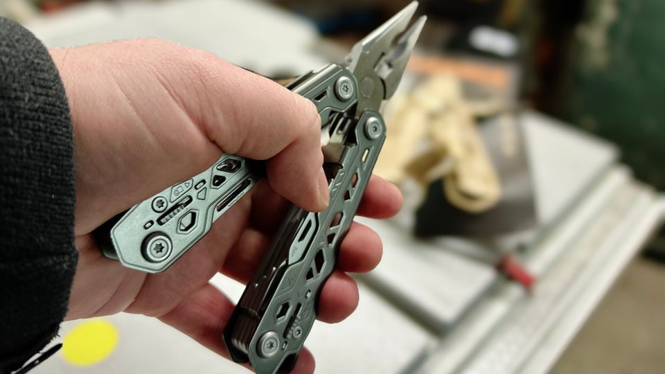 Das Gerber Truss Multitool wird geöffnet in der Hand gehalten, wobei die spitze Zange mit gezahnten Backen und der federbelastete Mechanismus sichtbar sind. Die robusten Edelstahlgriffe haben hexagonale Aussparungen für reduziertes Gewicht.