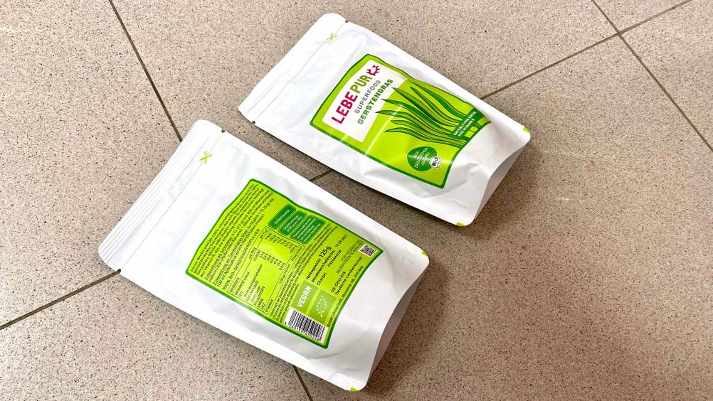 Zwei Packungen des Gerstengrases im Test, einmal liegt die Vorderseite oben, einmal die Rückseite inklusive Produktbeschreibung.