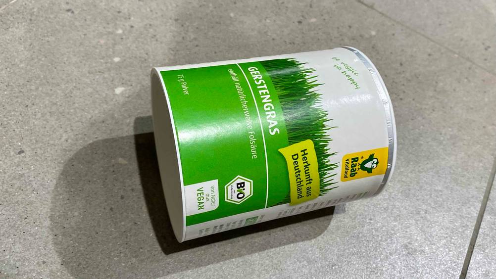 Eine Dose Gerstengras im Test liegt horizontal auf einem Fließenboden.