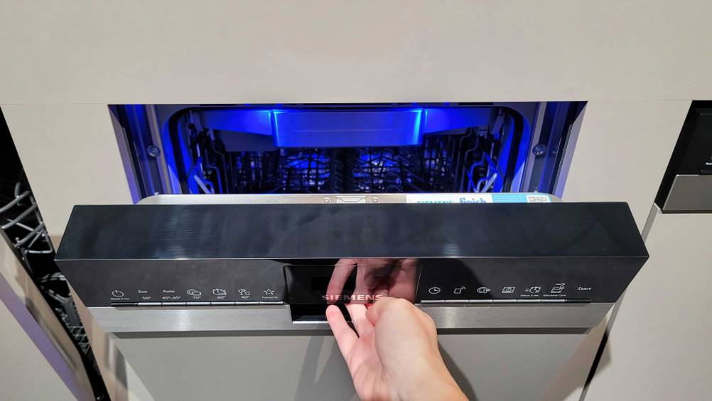 Eine Hand öffnet die Klappe eines teilintegrierten Geschirrspülers im Test.
