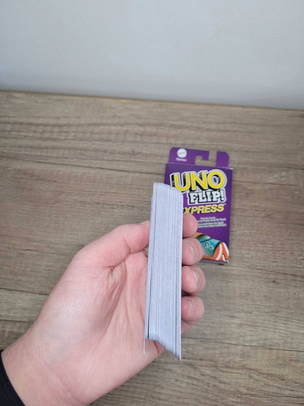 Gesellschaftsspiele getestet: Eine Hand hält ein Bundel Karten vor eine Packung Uno.