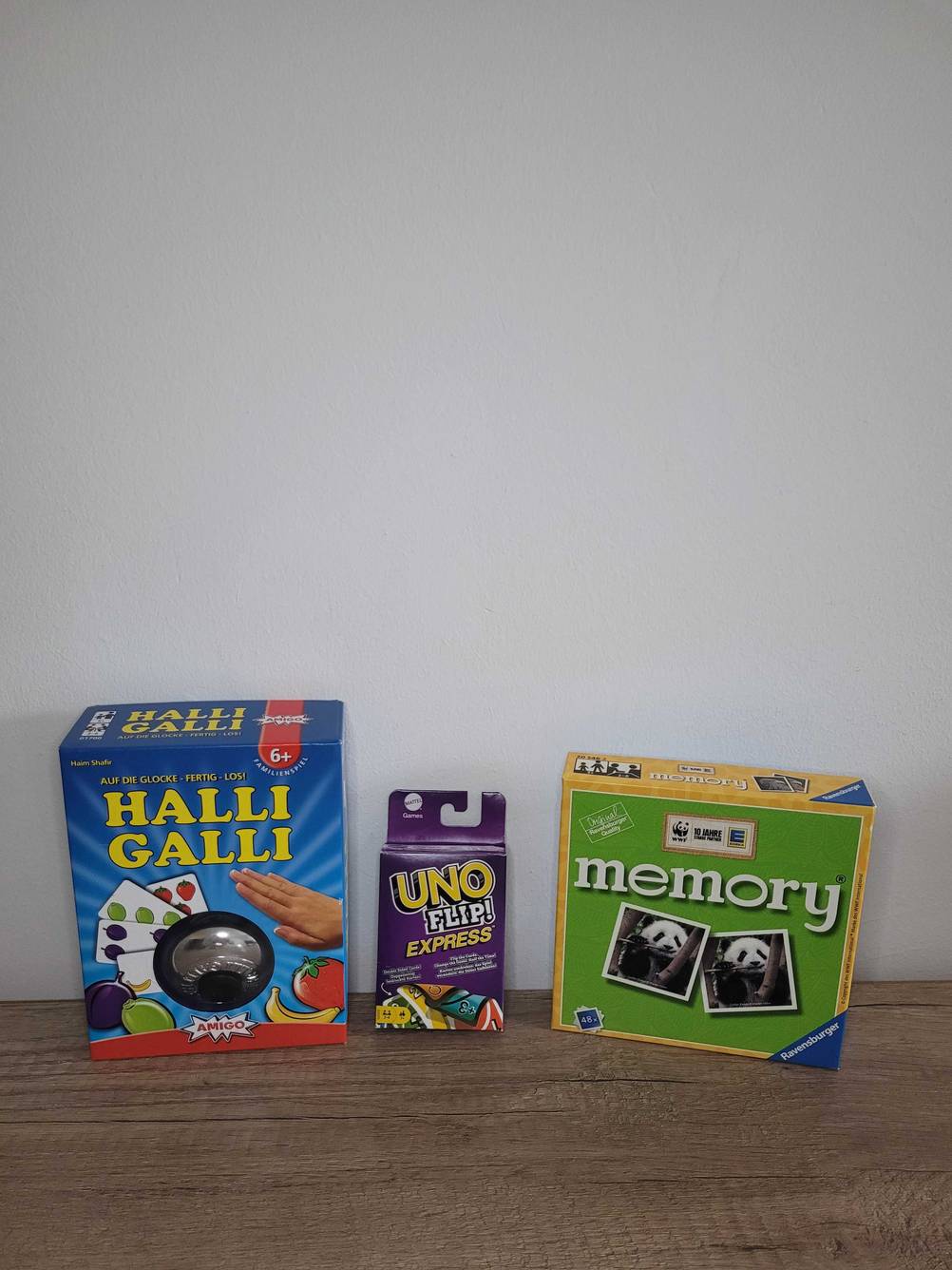 Gesellschaftsspiele getestet: Drei unterschiedliche Spiele, Halli Galli, Uno und Memory stehen vor einer hellen Wand.