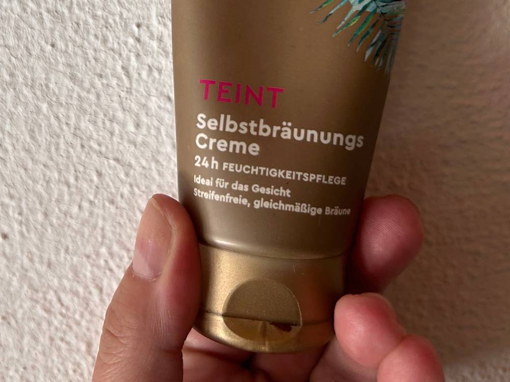 Nahaufnahme des Verschlusses einer Tube Gesichtsbräuner im Test von einer Hand gehalten.