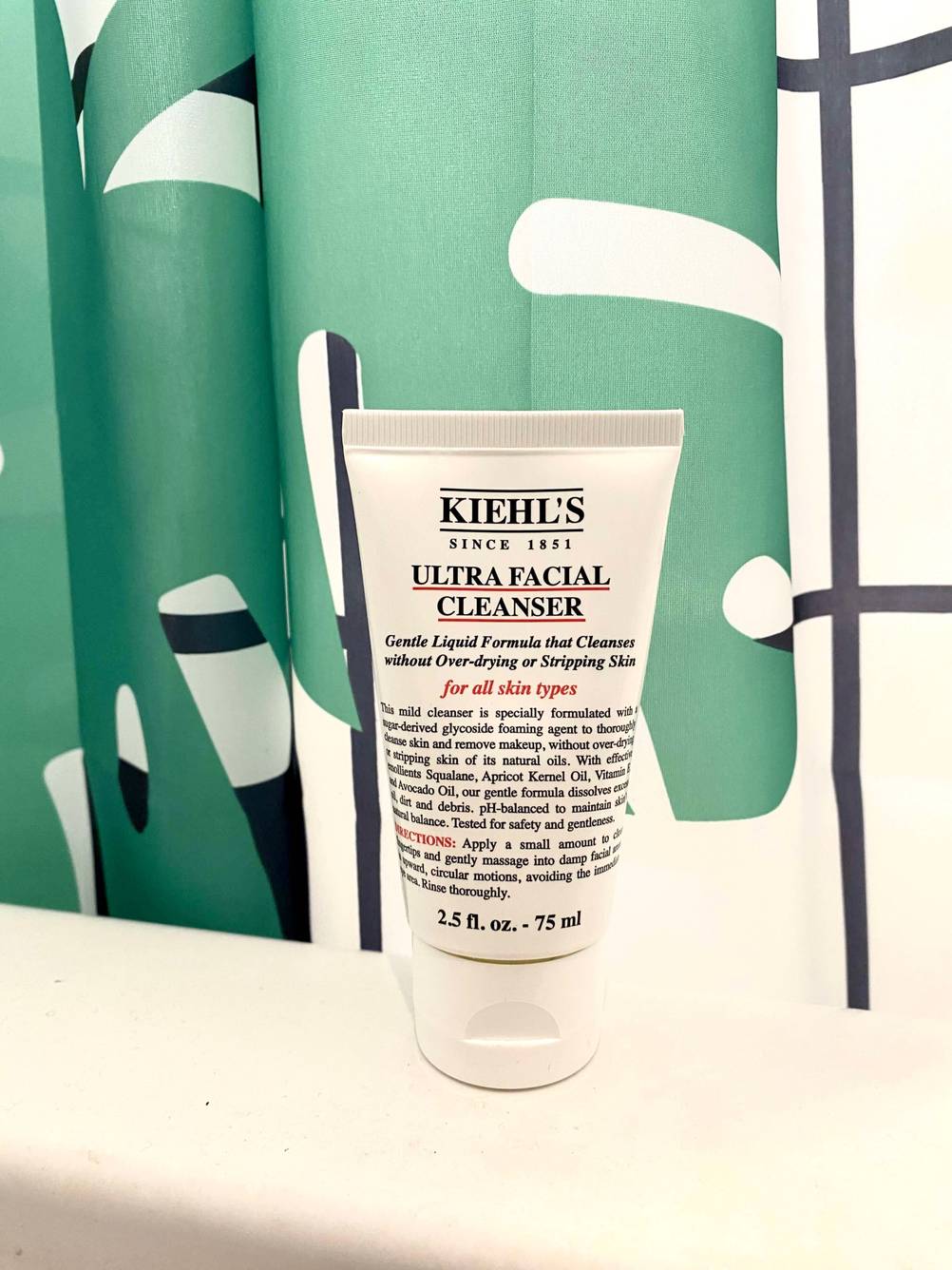 Eine Tube der getesteten Gesichtsreinigung steht vor einem Duschvorhang auf einem Badewannenrand.