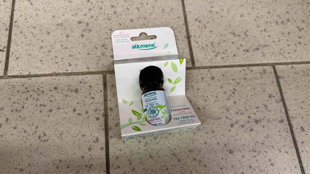 Eine Flasche mit veganem Alkmene Teebaumöl im Test liegt in seiner Verpackung auf dem Boden.