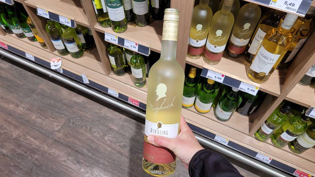 Eine Hand hält den getesteten Maybach-Wein in der Flasche mit Schraubverschluss vor einem Weinregal.