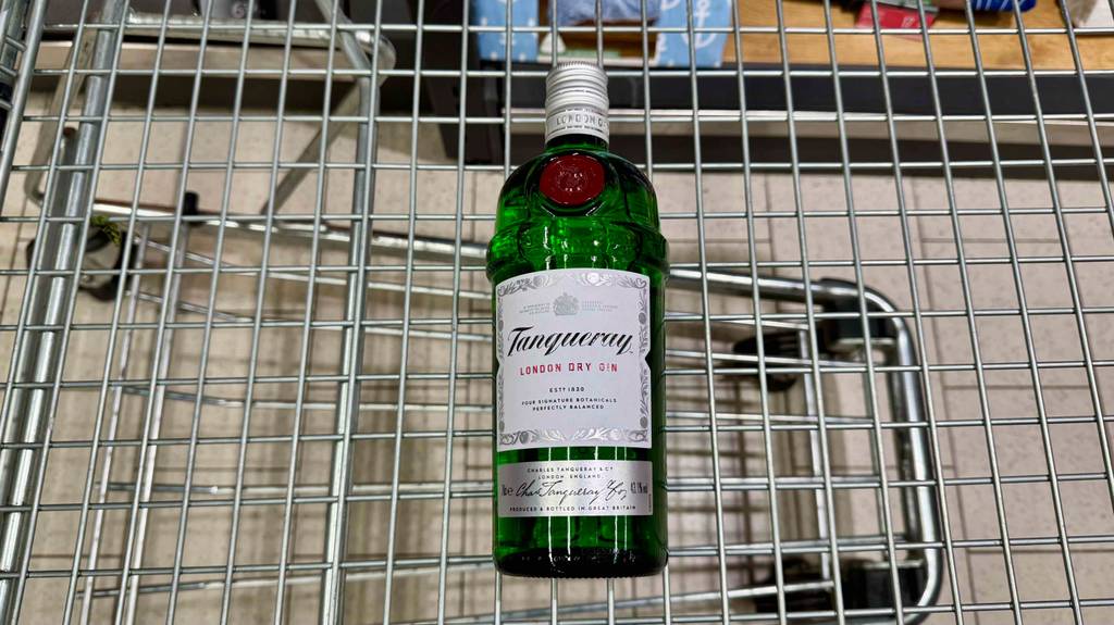 Ein getesteter Tanqueray-Gin in der grünen Flaschen mit Schraubverschluss liegt auf einem Regalgitter.