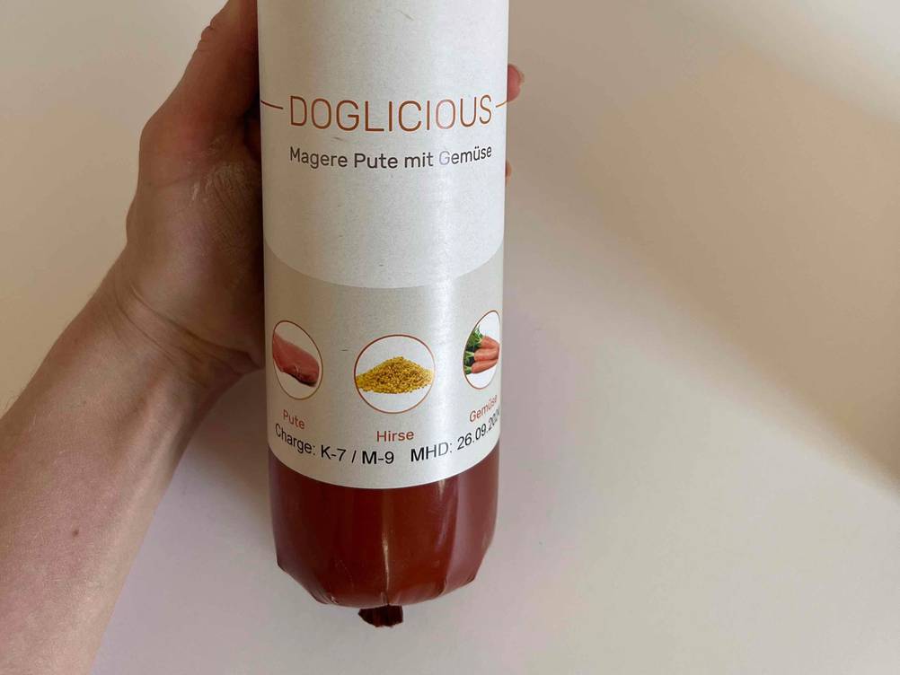 Getreidefreies Hundefutter getestet: Eine Hand hält eine Wurst mit Label.