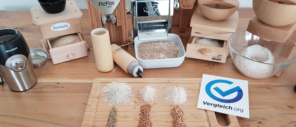 mehrere Getreidemühlen im Vergleich auf einem Tisch mit Auffangschale und Getreide