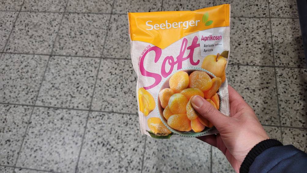 Eine Hand hält eine Packung getrockneter Aprikosen im Test hoch.