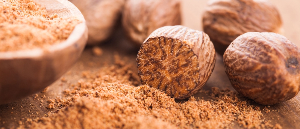Muskatmühle im Test: ganze Muskatnüsse und geriebene Muskatnuss auf einer Holzoberfläche