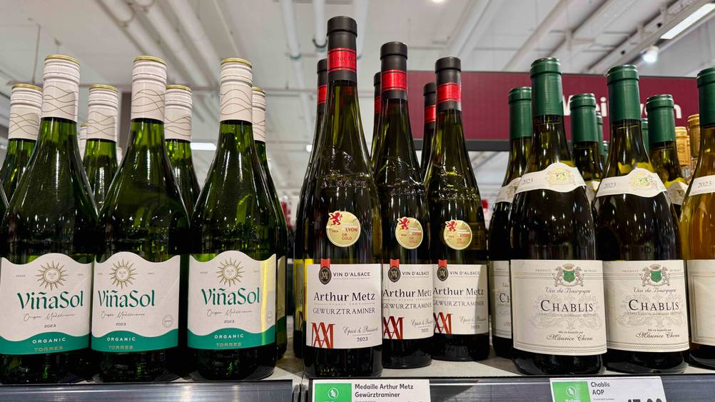 Mehrere Flaschen des Gewürztraminer im Test neben anderen Produkten in einem Verkaufsregal.
