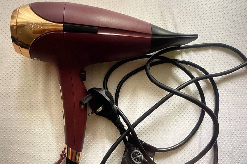 Haartrockner im Test: dunkelroter Haartrockner von ghd inklusive schwarzem Kabel auf hellem Untergrund.