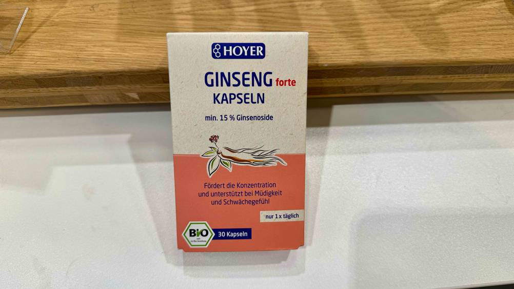 Eine Packung der getesteten Ginseng-Kapseln lehnt an einem Holzstück.