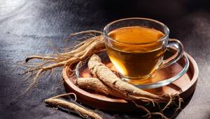 Ginseng-Tee-Test: Ein Teeglas mit Ginseng-Tee, daneben liegen frische Ginseng-Wurzeln. 