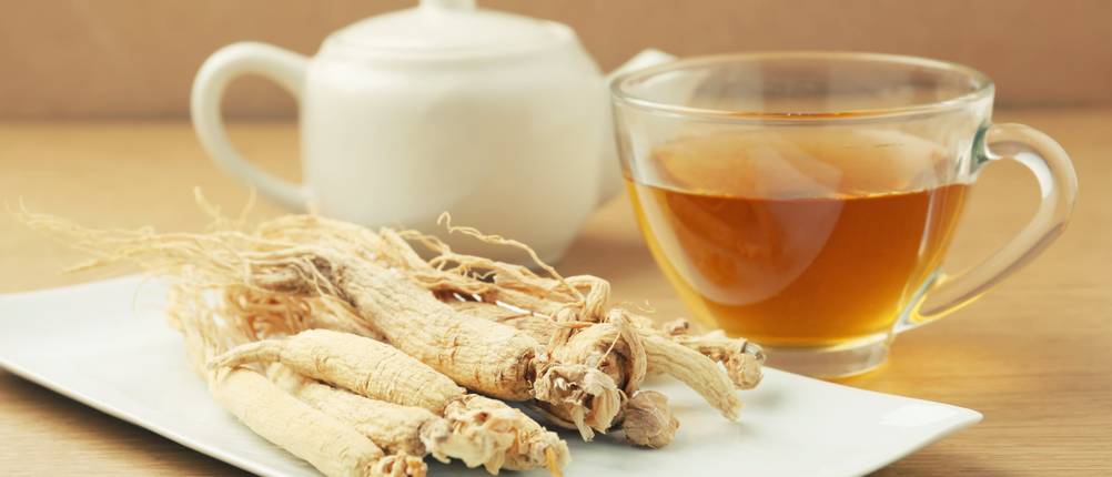 ginseng-tee-test: Auf einem Teller liegen Ginseng-Wurzeln. Daneben stehen ein Glas mit Tee und eine Teekanne. 