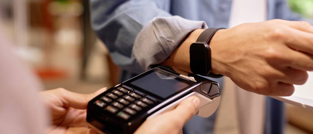 Kinderkonto-Vergleich: Ein junger Mann bezahlt an der Kasse mit seiner Smartwatch.