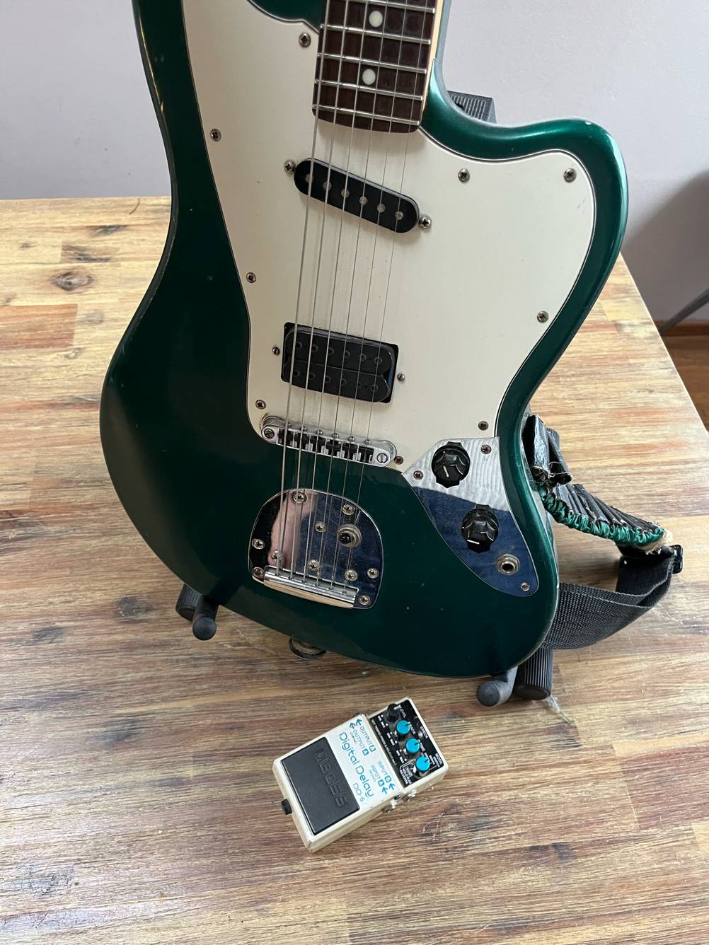 Vor einer Gitarre in einem Ständer liegt ein getestetes Gitarren-Effektgerät.