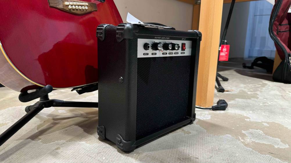Ein getesteter Gitarrenverstärker von schräg seitlich vor einer Gitarre auf dem Boden.