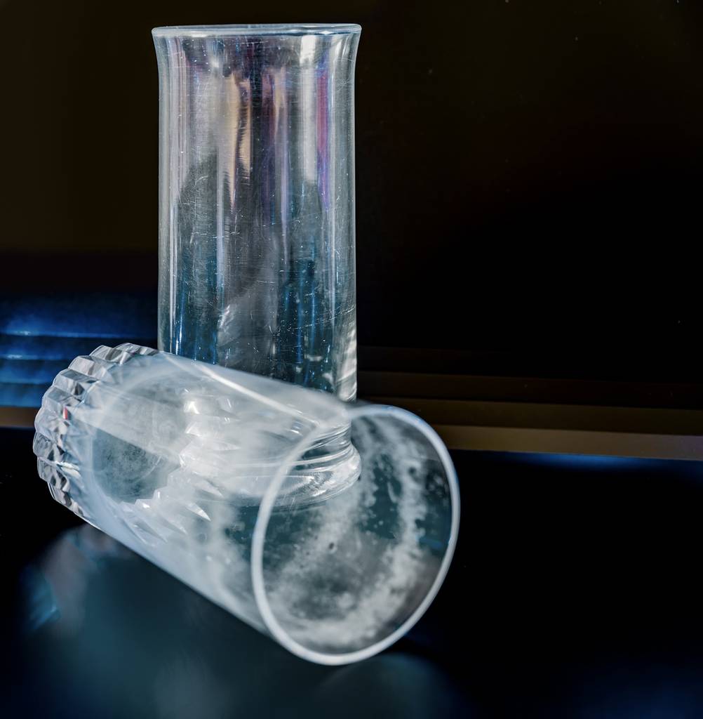 Ein stehendes und ein liegendes Glas, die beide von Glaskorrosion gezeichnet sind.