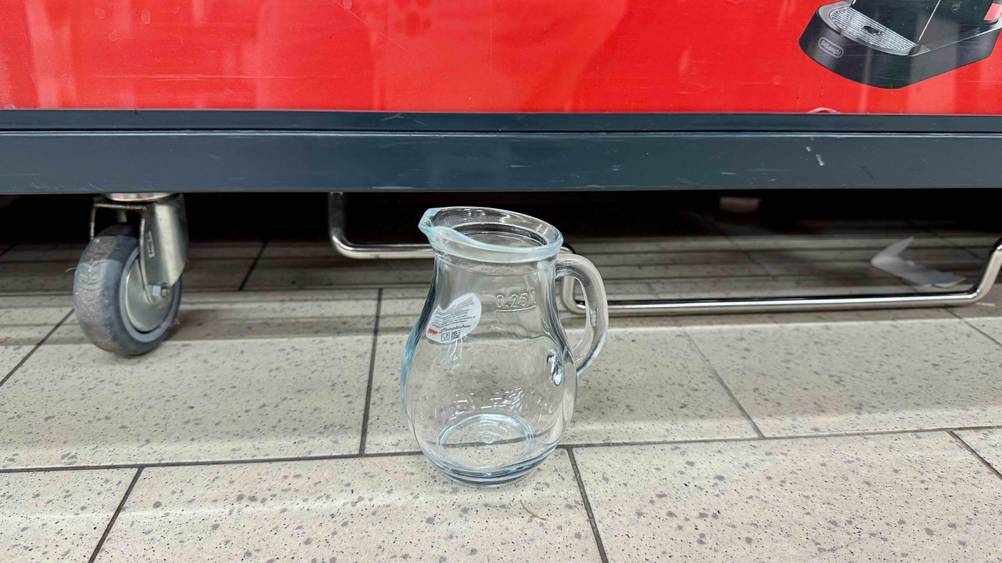 Ein Glaskrug im Test steht vor einem Rollwagen auf dem Boden.