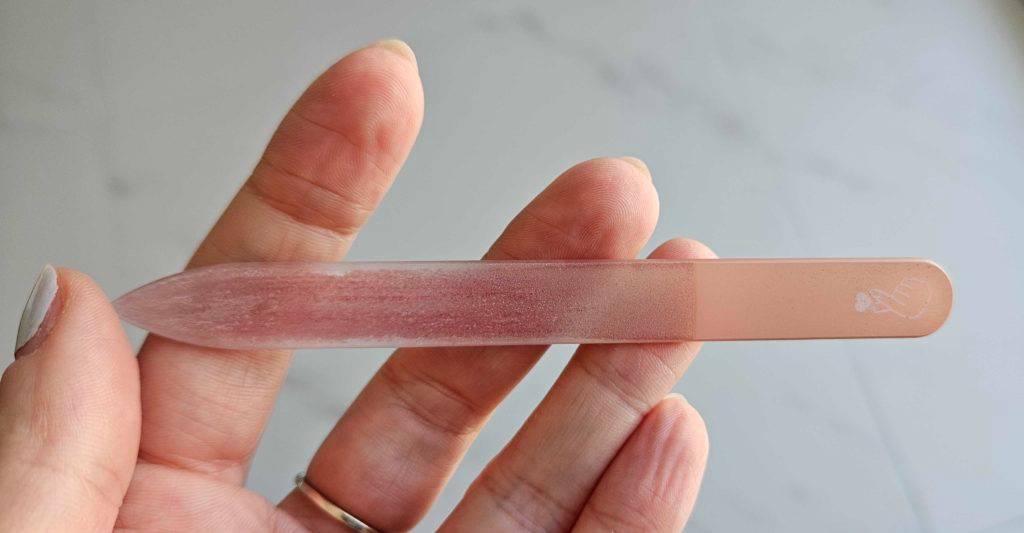 Getestete Glasnagelfeile in Rosa in einer Hand vor einer hellgrauen Fläche.