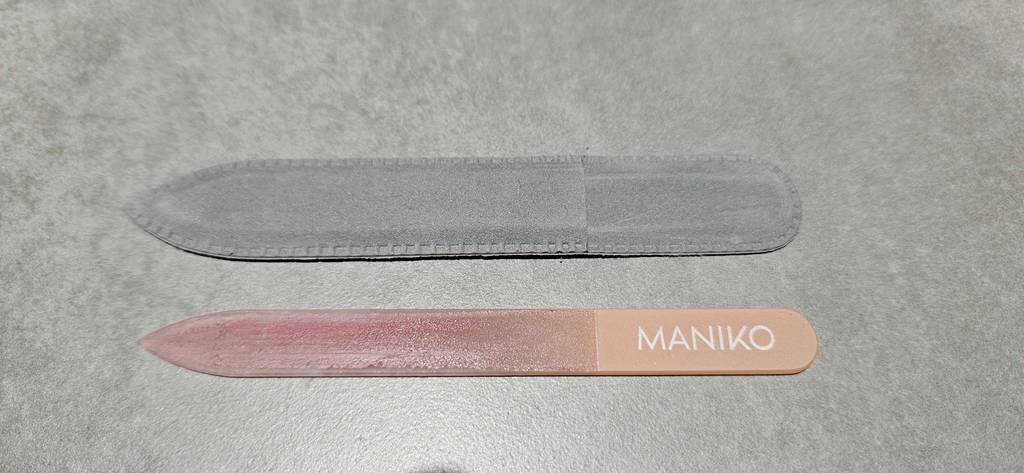 Maniko Glasnagelfeile im Test: rosa Modell liegt neben seinem grauen Aufbewahrungs-Etui auf einem hellgrauen Untergrund.