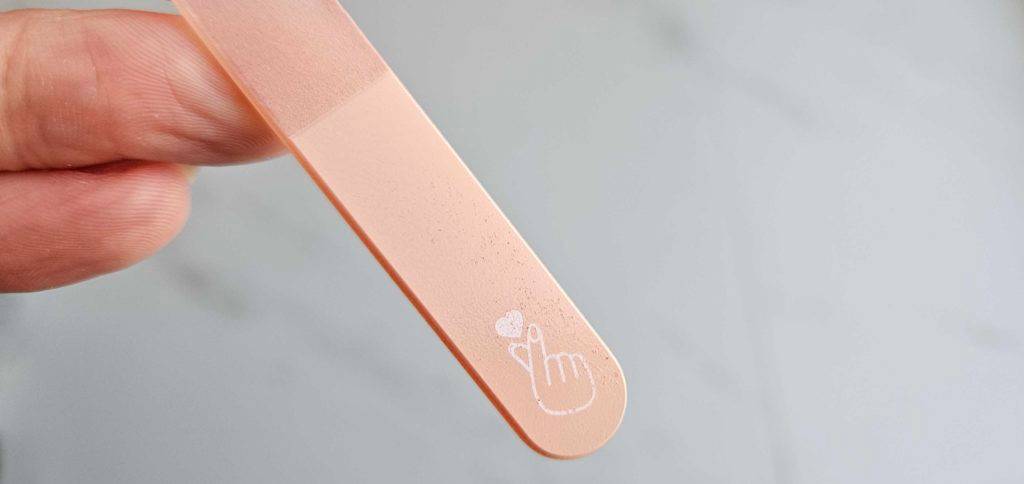 Nahaufnahme einer Glasnagelfeile im Test: Hand hält rosa Modell mit Markenzeichen vor einem hellgrauen Hintergrund.
