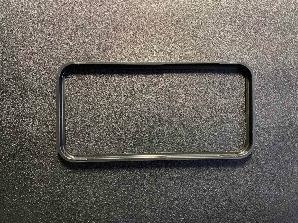 Ansicht von oben auf einen schwarzen Rahmen des Montage-Kits eines iPhone 12 Pro Panzerglases im Test auf schwarzer Fläche.