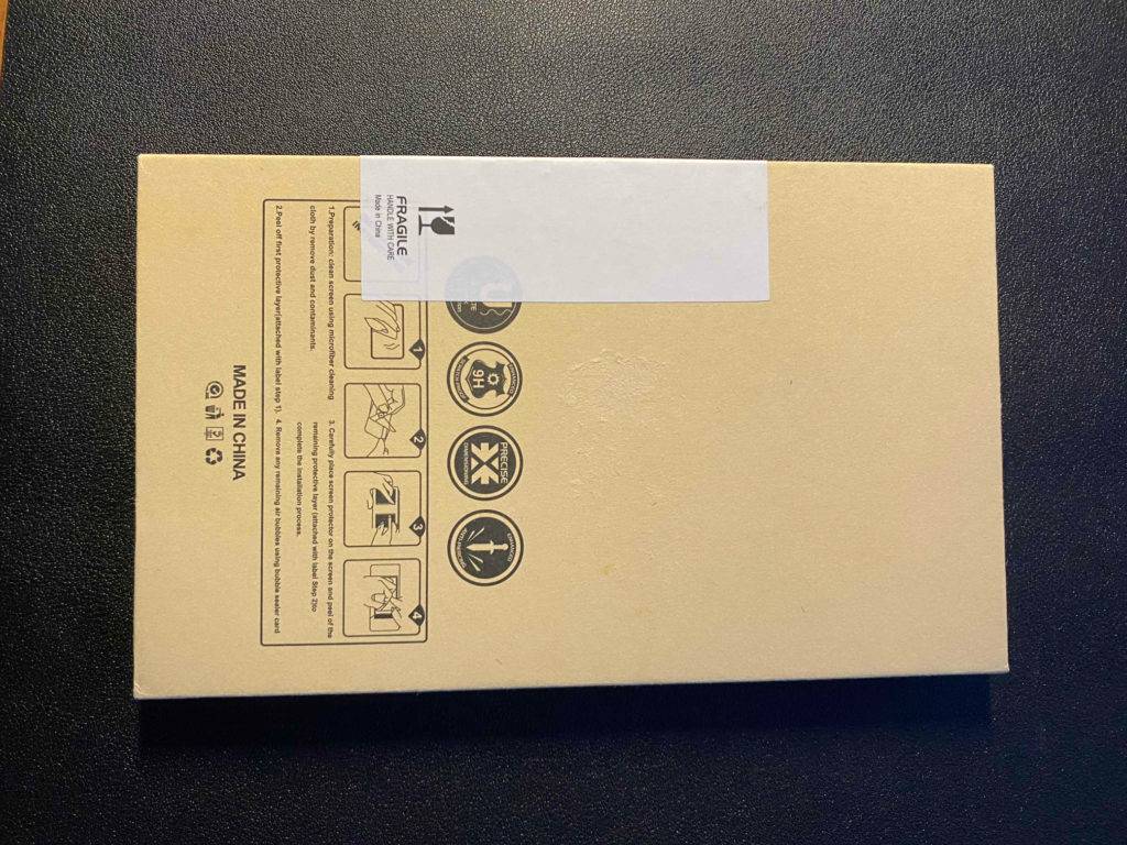 Rückwärtige Ansicht der beigefarbenen Verpackung eines iPhone 12 Pro Panzerglases im Test liegt auf einem schwarzen Untergrund.