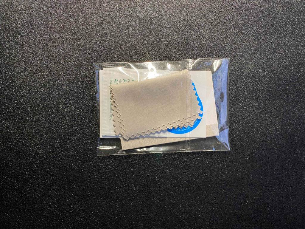 Ein Reinigungsset eines getesteten iPhone 12 Pro Panzerglases befindet sich in seiner Kunststoffhülle auf einem schwarzen Untergrund.