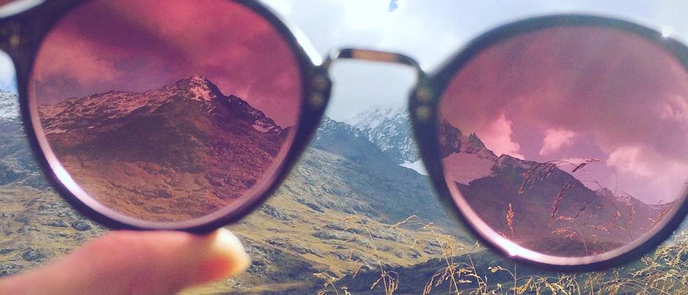 Gletscherbrille getestet: Rötlich-braun getönte Gletscherbrille mit runden Gläser vor einer Bergkulisse