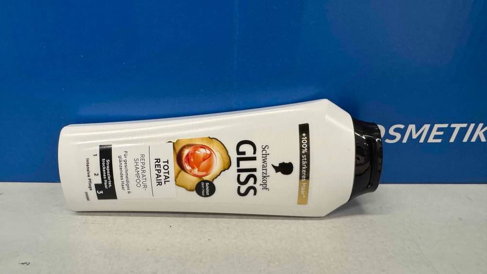 Vor einem blauen Karton liegt eine Flasche Gliss-Kur-Shampoo im Test horizontal.