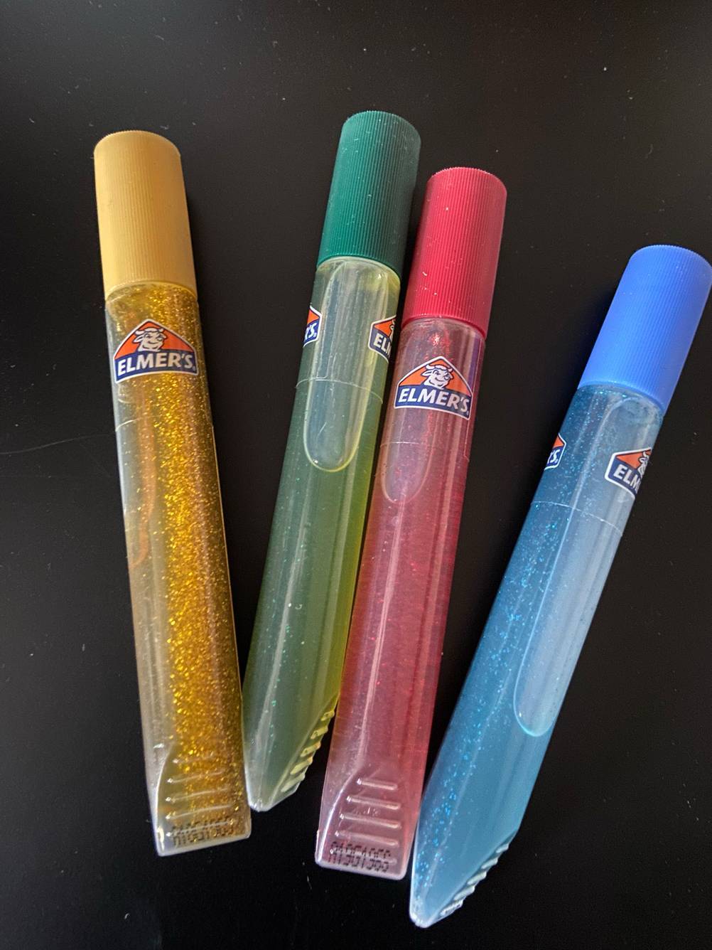 Vier Glitzerstifte im Test auf einer schwarzen Fläche.