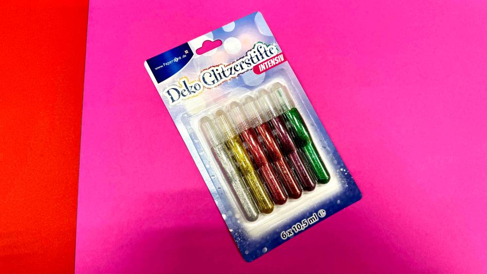 Auf einer pinken Fläche liegt eine Packung Glitzerstifte im Test.