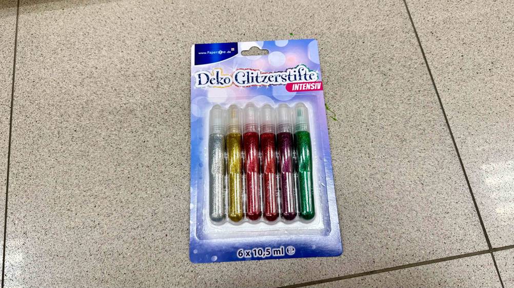 Getestet: Eine Packung Glitzerstifte befindet sich auf einem Fließenboden.