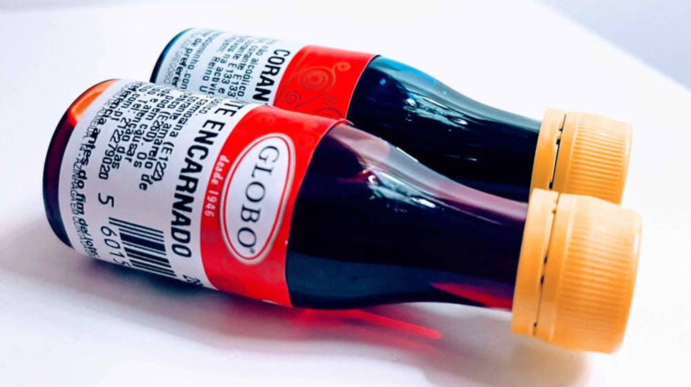 Zwei 28-ml-Flaschen inklusive getesteter Lebensmittelfarben liegen auf einer weißen Oberfläche.